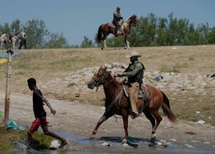 A United States Border Patrol agent on horseback tries to stop a Haitian migrant from entering an en...