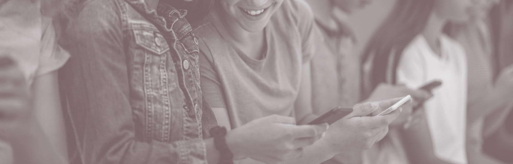 A group of multi-ethnic high school students sit together in a row. They are each dressed casually ...