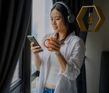 Young Asian woman is listening to music and holding a coffee cup in the living room.