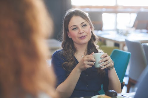 Young woman having lunch at a restaurant with friends, she hold cup with coffee