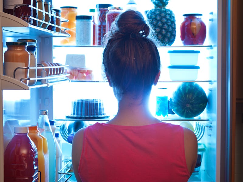 A woman standing in front of the open refrigerator at late night to get a snack