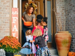 A diverse group of children, dressed in costumes, trick or treating in a residential USA neighborhoo...