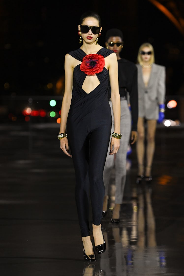 A model walking in a black Saint Laurent dress with a red flower on the runway