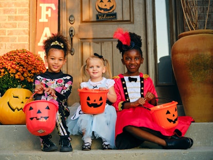 A diverse group of children, dressed in costumes, trick or treating in a residential USA neighborhoo...