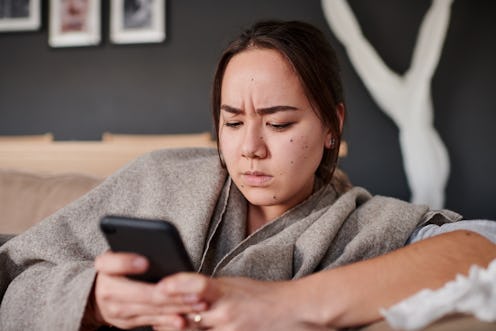 A woman stares at her phone stressed about texting a friend after an argument.