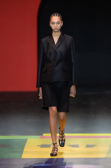 A model walking on the runway in an black jacket and skirt by Dior