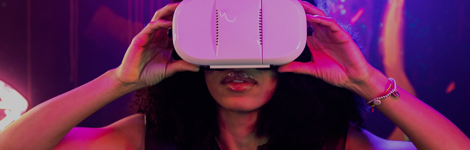 Young adult Afro American woman using Virtual Reality headset with both hands holding it at night wi...