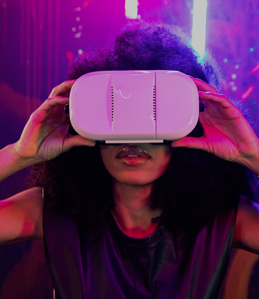 Young adult Afro American woman using Virtual Reality headset with both hands holding it at night wi...