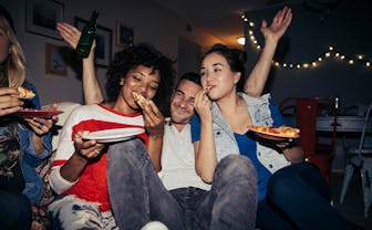 Two women and one man sitting on a couch eating pizza and partying.