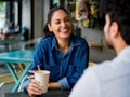 Happy Latin American woman on a date at a cafe talking to a man while drinking coffee and laughing -...