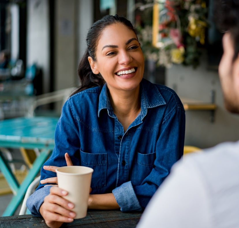 Happy Latin American woman on a date at a cafe talking to a man while drinking coffee and laughing -...