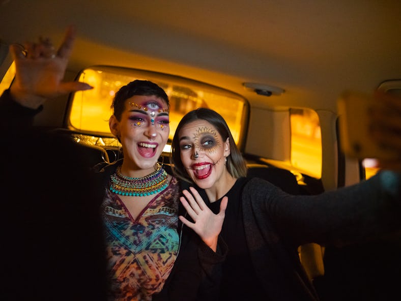 Two girls are taking a selfie in a car during a drive-thru Halloween experience. 