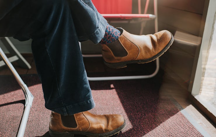 Relaxed scene of a man wearing brown leather Chelsea boots sitting in a sun room in front of an open...