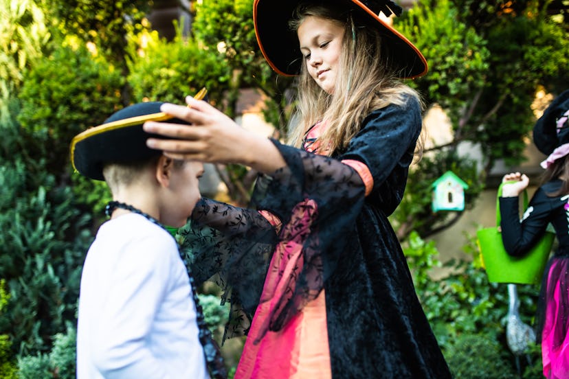 A pretty girl in a witch costume is straightening her cute brother's pirate hat while trick-or-treat...