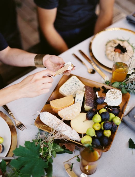 People eating cheese from a charcuterie board at a dinner party on a dime