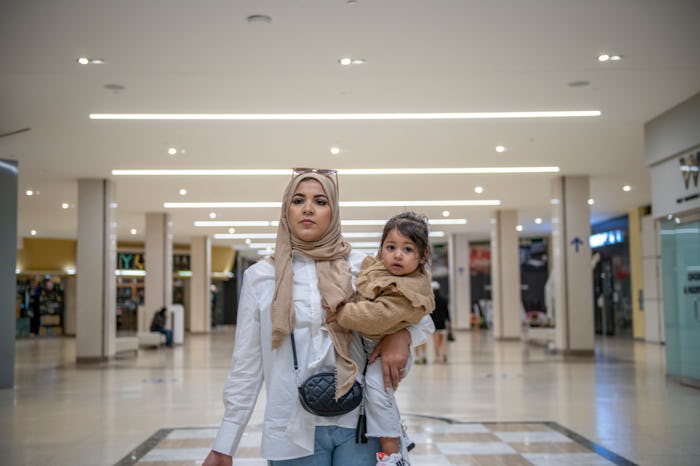 A young Muslim mother walks through an airport with her infant daughter in her arms on her hip. The...