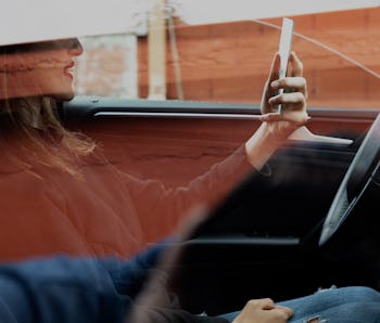 Outside view of a woman checking her makeup on a mirror while sitting in the driver seat of her car....