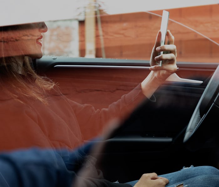 Outside view of a woman checking her makeup on a mirror while sitting in the driver seat of her car....