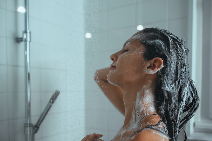 A young woman lathers her hair with shampoo as she takes a daily shower