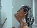 A young woman lathers her hair with shampoo as she takes a daily shower