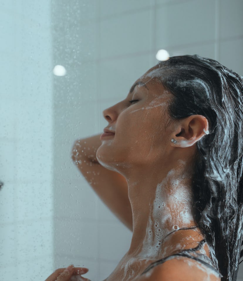 A young woman lathers her hair with shampoo as she takes a daily shower