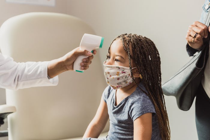 An unrecognizable healthcare professional checks a young female patient's temperature with an infrar...