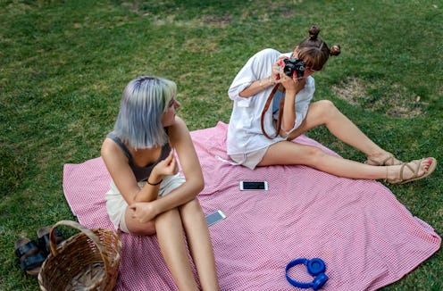 Two women take photos of each other on a picnic blanket, drifting apart as friends.