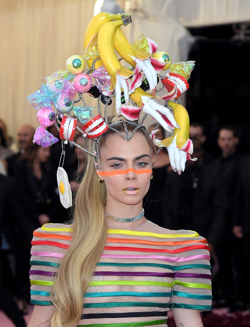 Cara Delevingne keeps her makeup pared down at the 2019 Met Gala — except for a neon stripe across h...