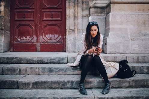 Vintage toned image of a young Parisian woman checking cellphone while sitting on the stairs in the ...