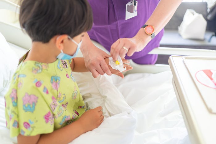 Nurse removing IV from the hand of a little patient child on hospital bed