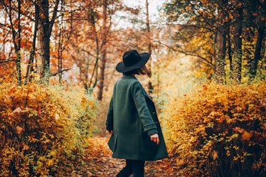 Girl in hat standing back at autumn forest in October 2021, the worst month for her zodiac sign.