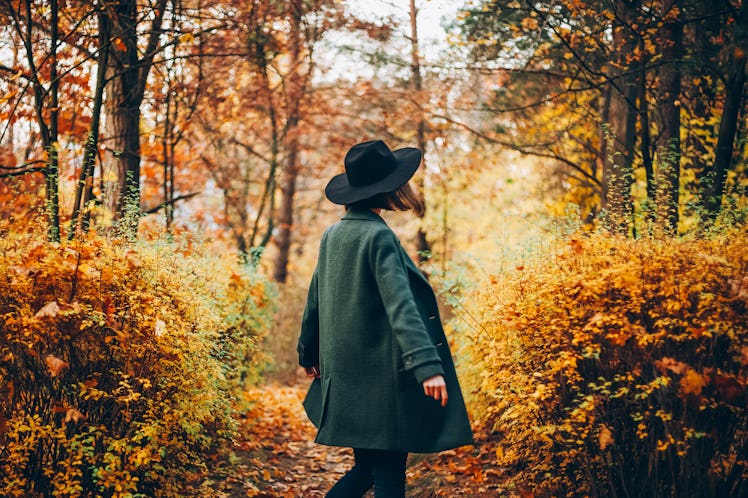 Girl in hat standing back at autumn forest in October 2021, the worst month for her zodiac sign.