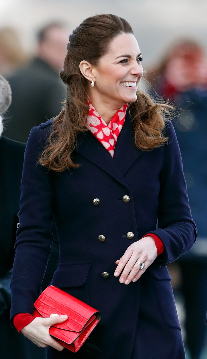 Kate Middleton wears a navy coat and red scarf.