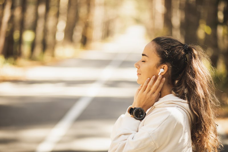 Pretty and attractive woman listening music in wireless earpods. Enjoying and preparing for running ...