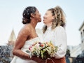two women smile at each other during their wedding, one of the best days to get married in 2022 acco...
