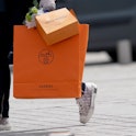 PARIS, FRANCE - MAY 11: A passerby wears Dior B23 sneakers and holds a Hermes orange shopping paper ...