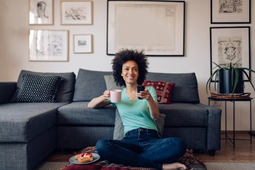 Young Afro woman enjoying a weekend morning, drinking coffee and watching TV