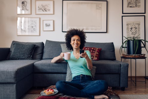 Young Afro woman enjoying a weekend morning, drinking coffee and watching TV