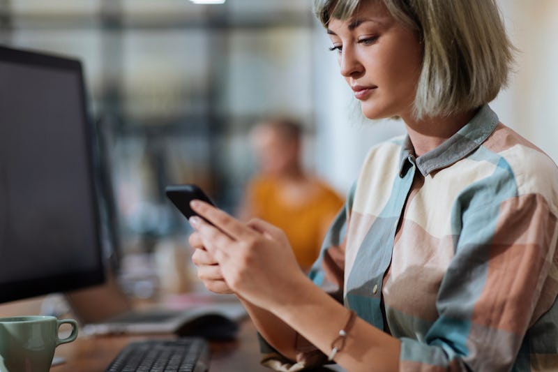 Beautiful young blond woman using her mobile phone while sitting in an office