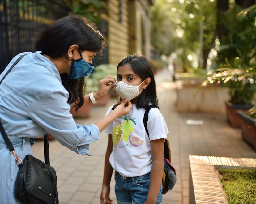 Mother putting mask on daughter's face while walking on pedestrian walkway the Mumbai city street