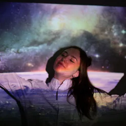 A woman stands in front of a projection of an aurora borealis. Here are 2022 vision board ideas, acc...