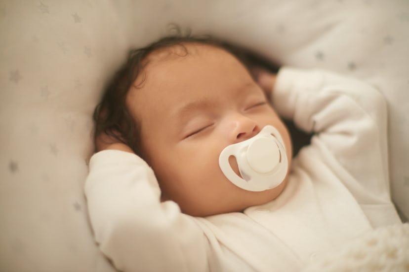 infant sleeping with its arms up; sucking on paci
