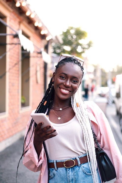 Pretty young african american woman walking in city at summer and using smart phone at street.