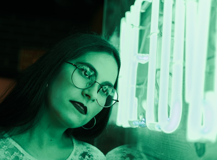 Young woman leaning her head against neon green sign, thinking about how January 17, 2022 will be th...