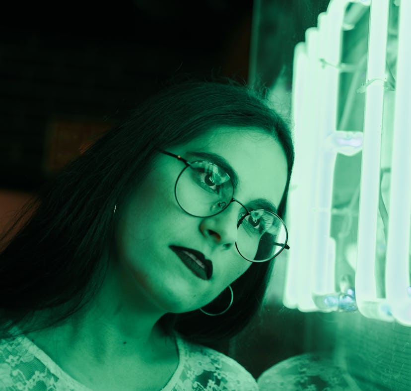 Young woman leaning her head against neon green sign, thinking about how January 17, 2022 will be th...