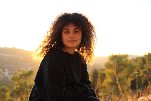 a woman stands in a field at sunset. Cancer, Sagittarius, and Pisces zodiac signs will be least affe...