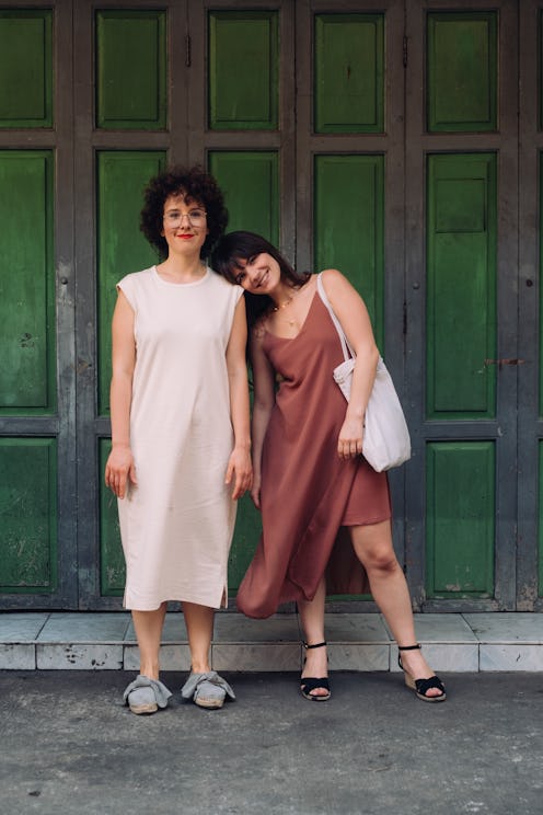 Two smiling women standing outside a green gate.