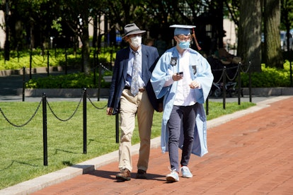 Absolventą su kepure, chalatu ir apsaugine kauke galima pamatyti Kolumbijos universiteto miestelyje ...