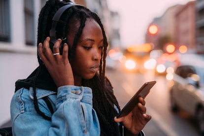 Young woman listening to her headphones, reading about how January 24, 2022 will be the worst week f...