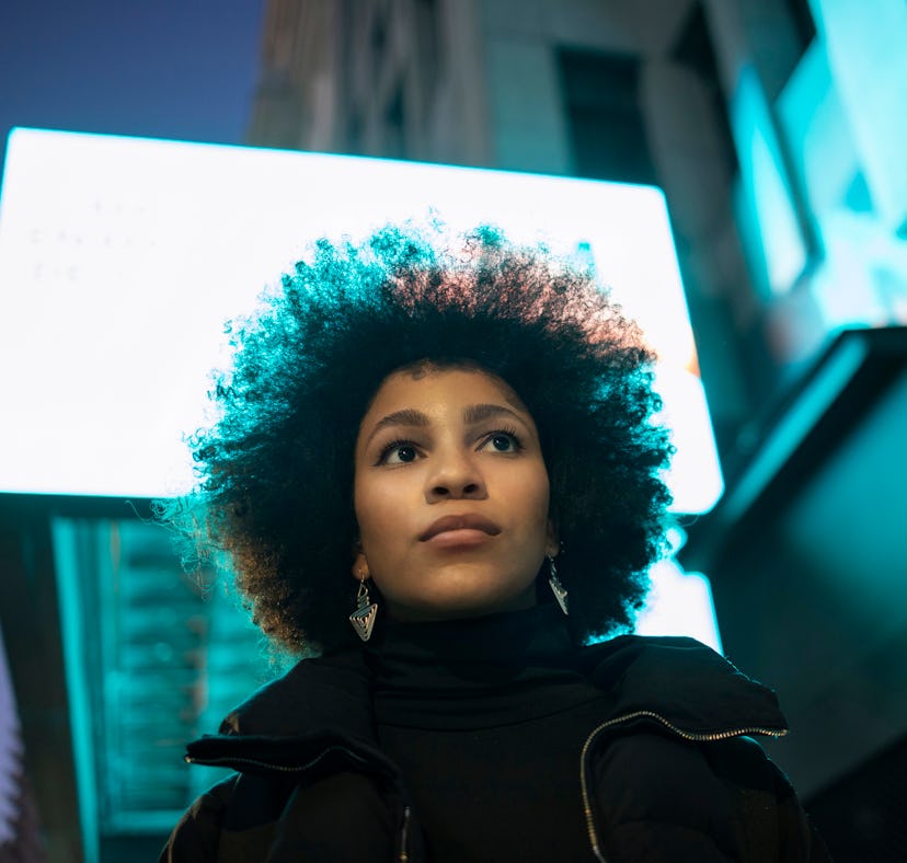 Young woman standing in front of blue street light, thinking about how January 24, 2022 will be the ...
